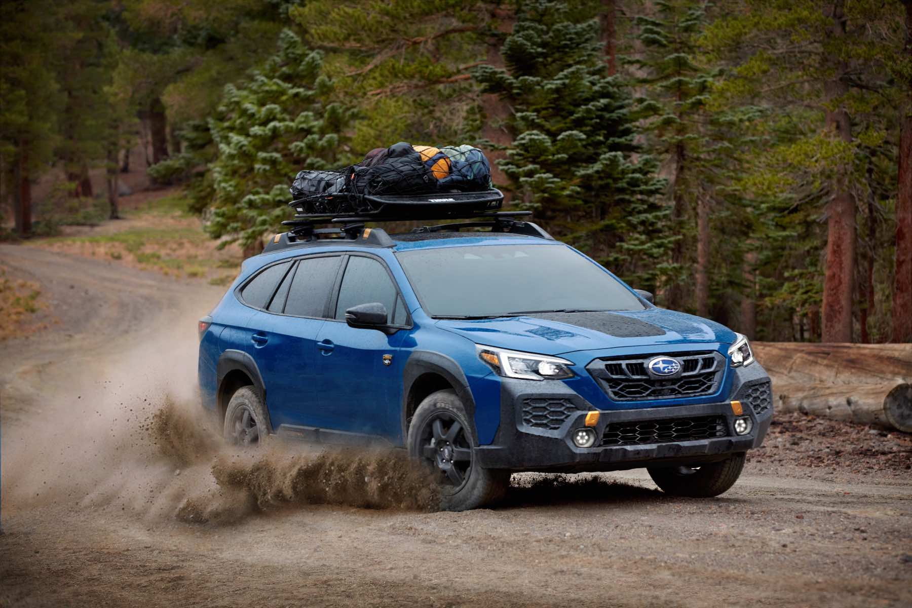 A blue 2024 Subaru Outback drives vigorously off-road. It's one of the new 2024 Subaru SUVs.