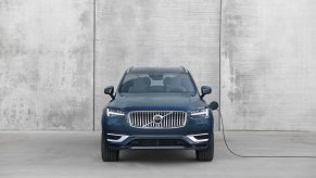 A blue 2023 Volvo XC90 Recharge plugged in while parked in front of a gray wall.