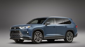 A blue 2024 Toyota Grand Highlander in front of a grey background. It's a new three-row Toyota SUV.