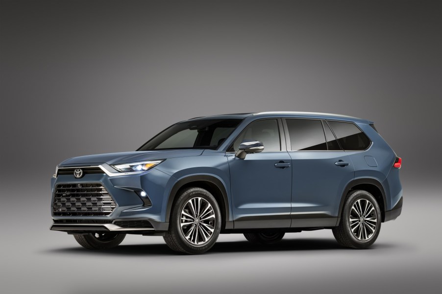 A blue 2024 Toyota Grand Highlander in front of a grey background. It's a new three-row Toyota SUV.