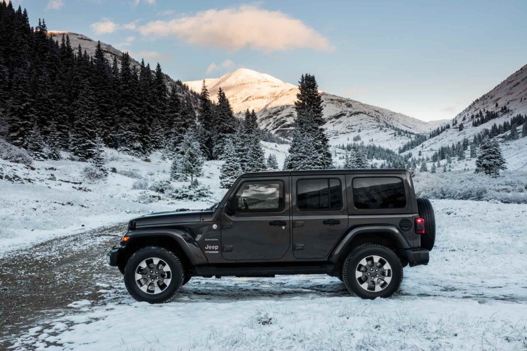 Side profile view of a 2023 Jeep Wrangler Sahara sits amid snow and mountains.