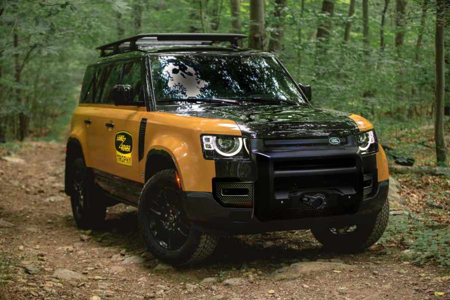 The Land Rover Defender Trophy Edition sits in a green forest. It's a new off-road SUV on the market.