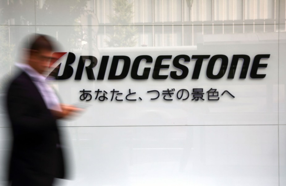 A man walks by the Bridgestone logo written in both English and Japanese, on a white wall.