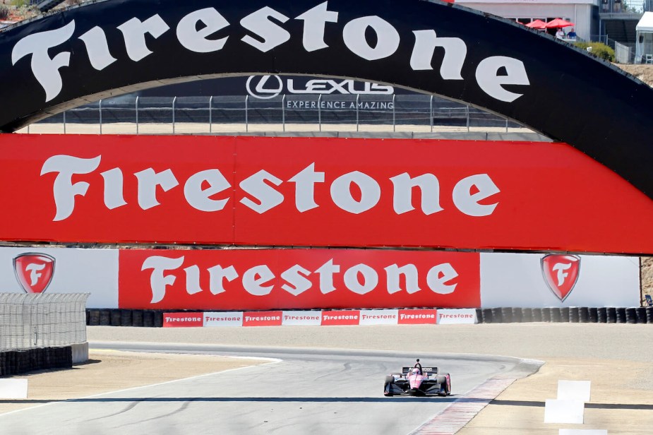 A Grand Prix car driving under a huge Firestone sign at the Monterrey race track.
