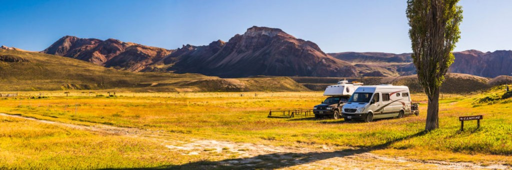 RVs parked in open wilderness area with mountains behind