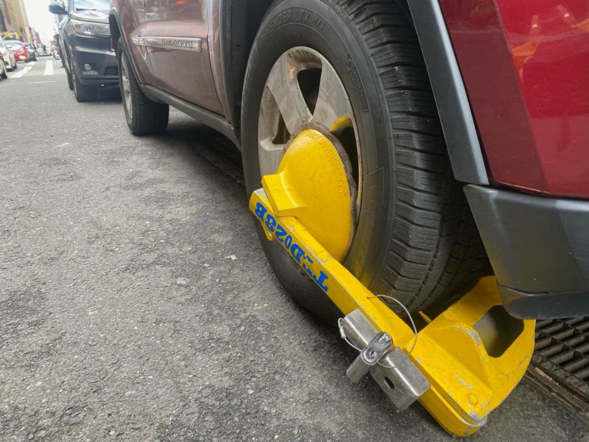 A boot on the tire of a car parked on a city street.