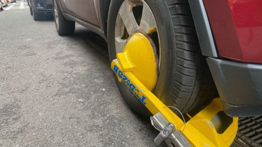 A boot on the tire of a car parked on a city street.