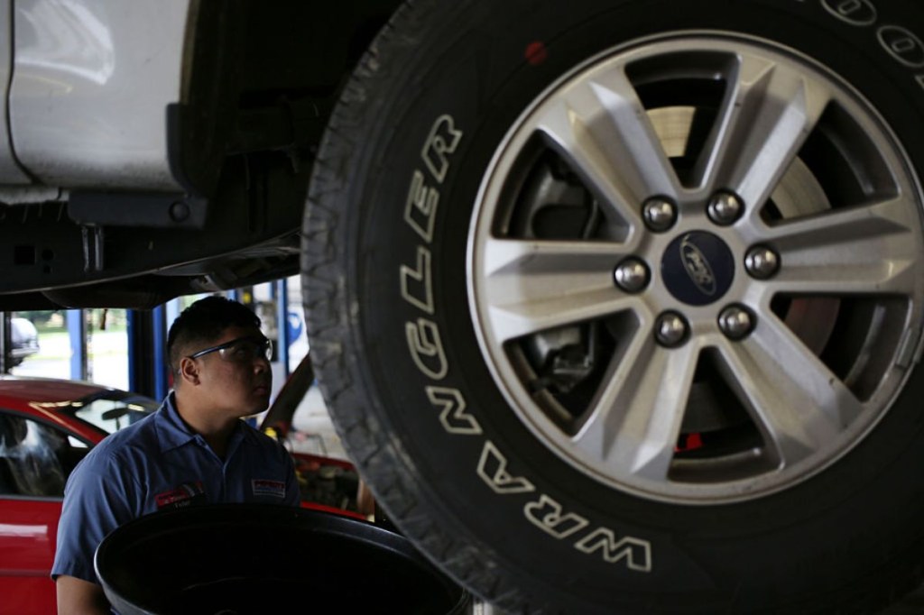 A car mechanic inspects the underside of a car to see if the axles are okay.