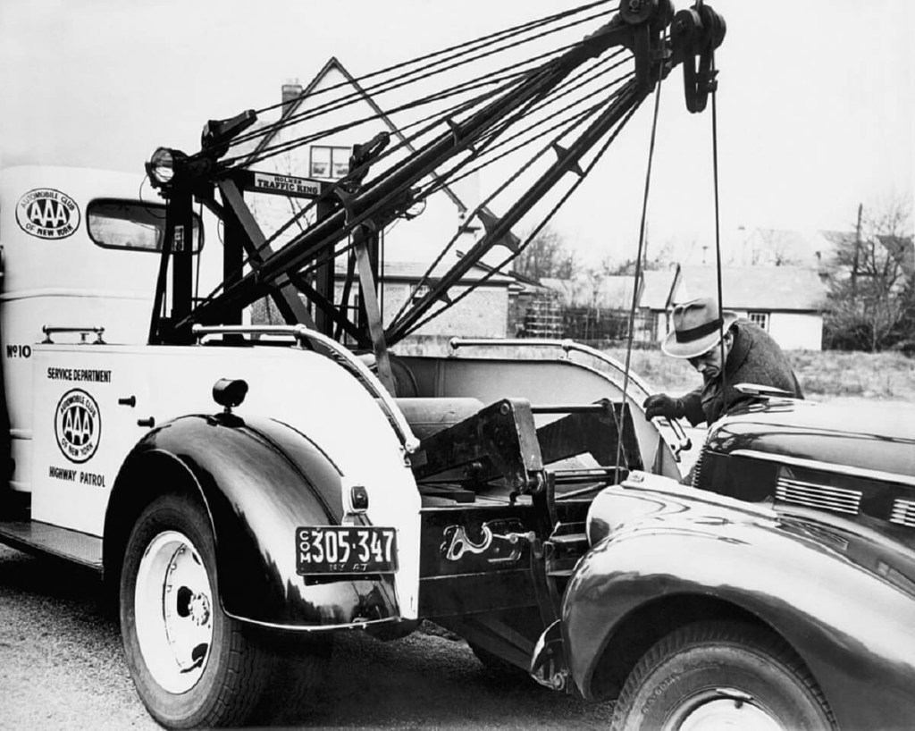 A black and white tow truck provides roadside assistance and towing to a car after a breakdown. 