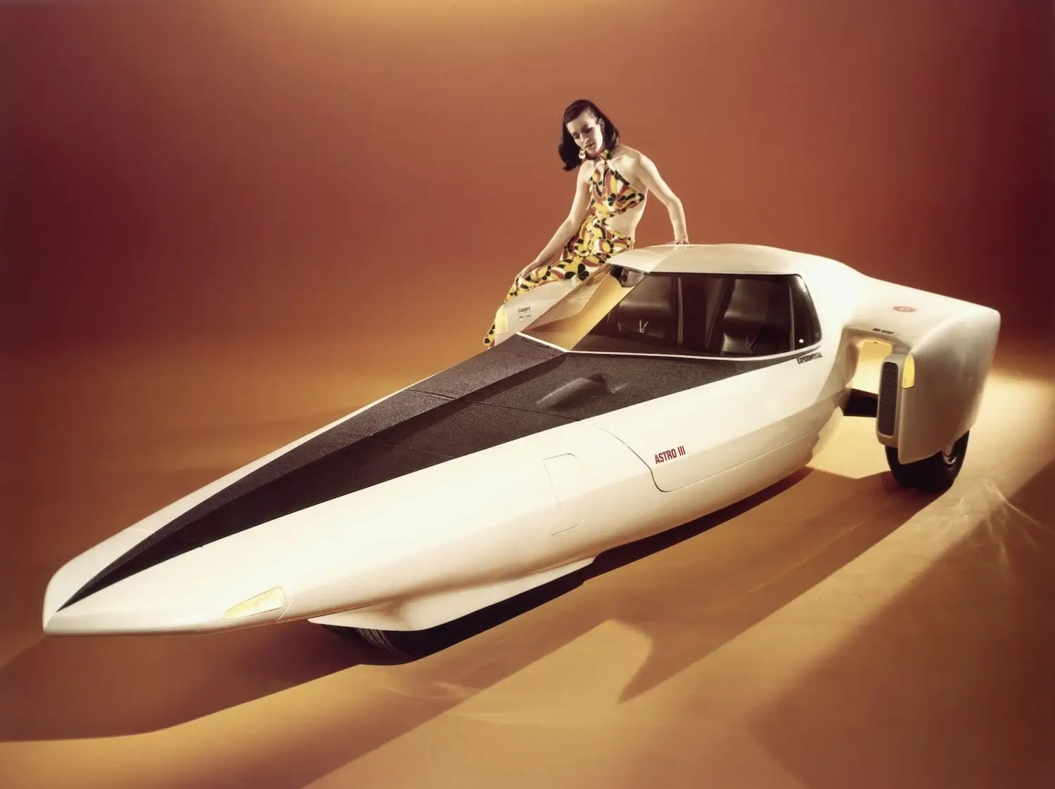 A model sits on the fender of a futuristic, rocket-shaped 1969 Chevrolet prototype at an auto show.