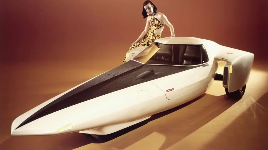 A model sits on the fender of a futuristic, rocket-shaped 1969 Chevrolet prototype at an auto show.