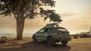 The 2024 Subaru Crosstrek faces away from the viewer overlooking the ocean at sunset with a tree in the foreground.