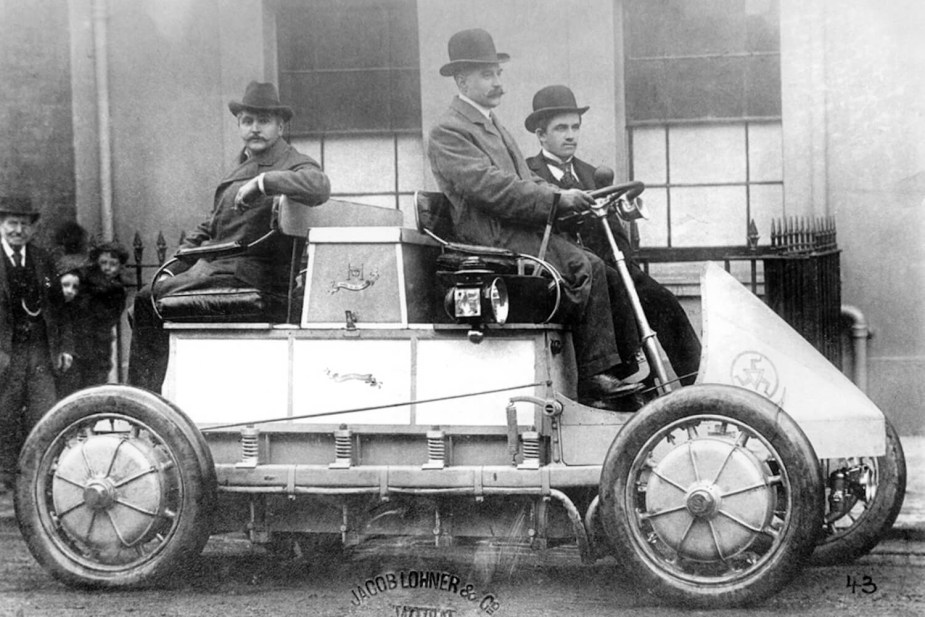 Three men in bowler hats atop an AWD electric vehicle in 1901.