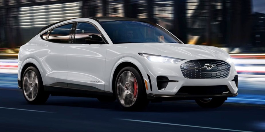 A white 2023 Ford Mustang Mach-E small electric SUV is driving on the road. 