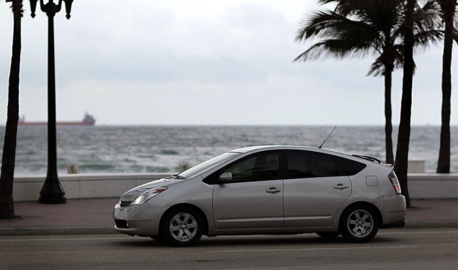 A silver Toyota Prius hybrid model cruises by the coast. 