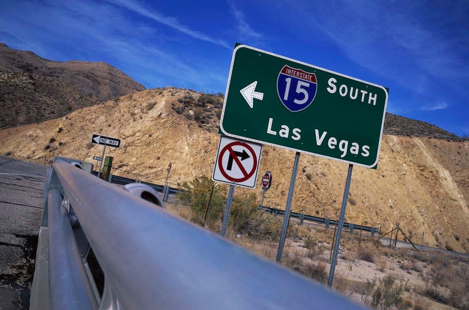 A sign for the I-15 interstate highway south towards Las Vegas, a sandy cliff visible in the background.