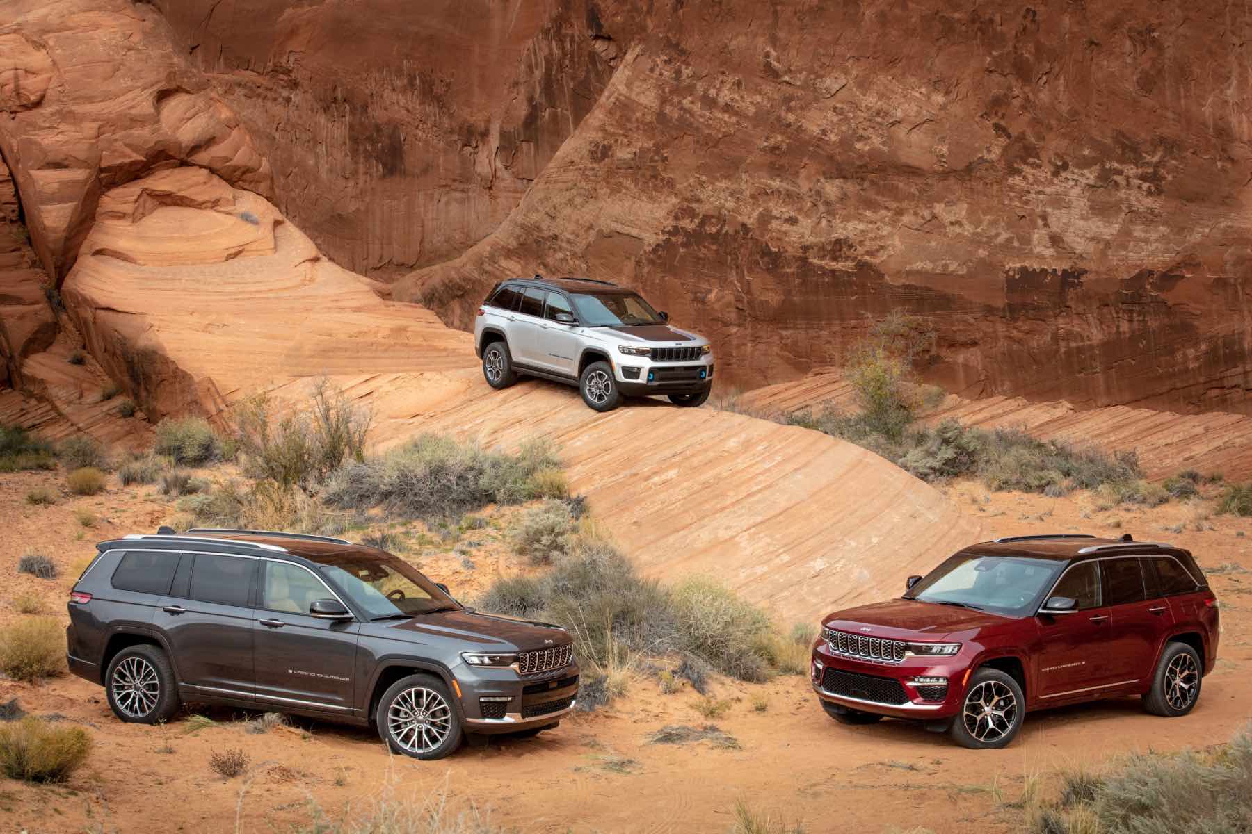 Three different Jeep Grand Cherokee models sit amid red rock formations.