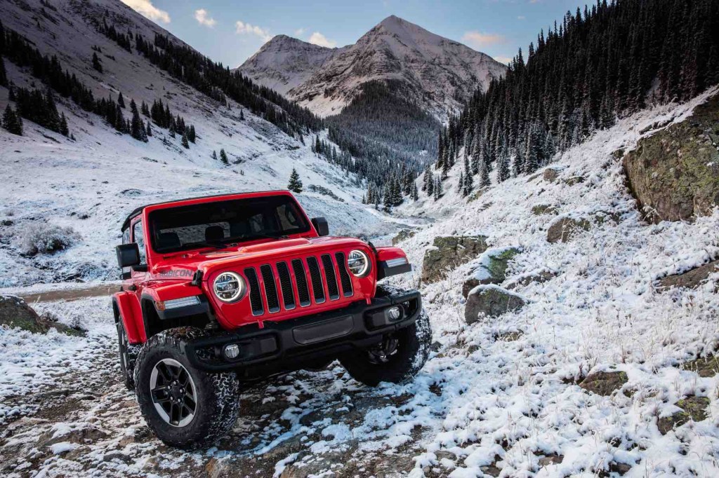 A red Jeep Wrangler shows its winter performance by climbing up a mountainside covered in snow. 