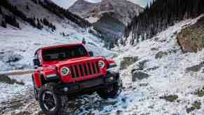 A red Jeep Wrangler shows its winter performance by climbing up a mountainside covered in snow.
