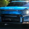 A blue 2023 Kia EV9 midsize electric SUV is driving on the road.