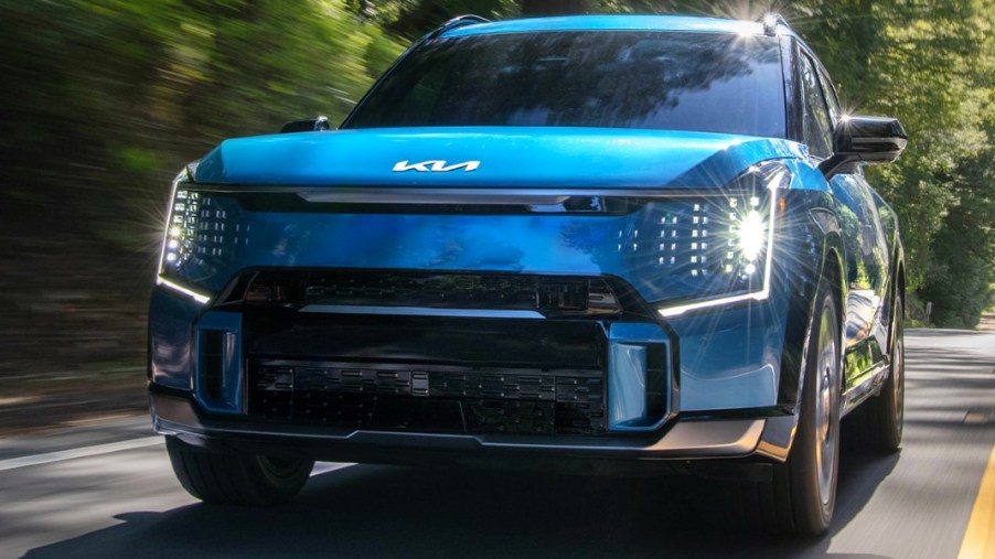A blue 2023 Kia EV9 midsize electric SUV is driving on the road.
