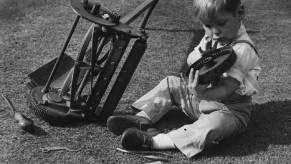 A young boy rolls over a lawn mower and repairs it.