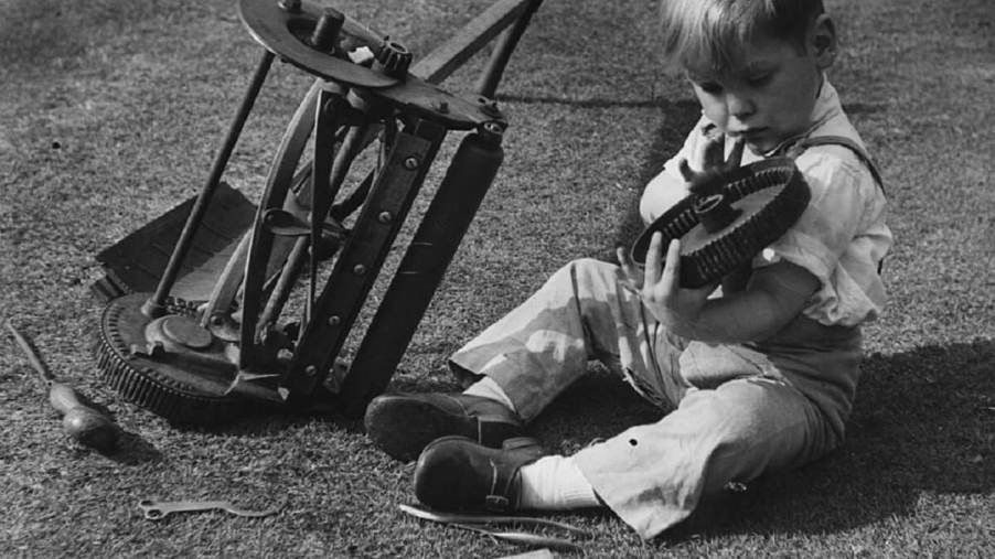 A young boy rolls over a lawn mower and repairs it.
