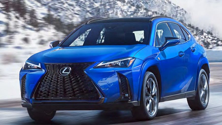 A blue 2023 Lexus UX subcompact luxury SUV is driving on the road.