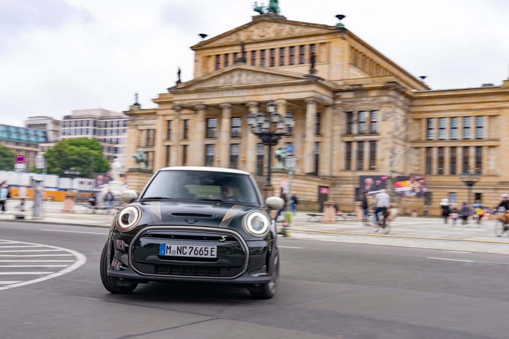 A green Mini Electric Hardtop, the electric version of the Mini Cooper, corners in a city. 