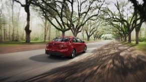 a red Toyota Corolla Hybrid driving through a tree-lined road
