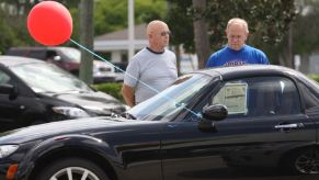 Two older potential owners inspect a Mazda MX-5 Miata.