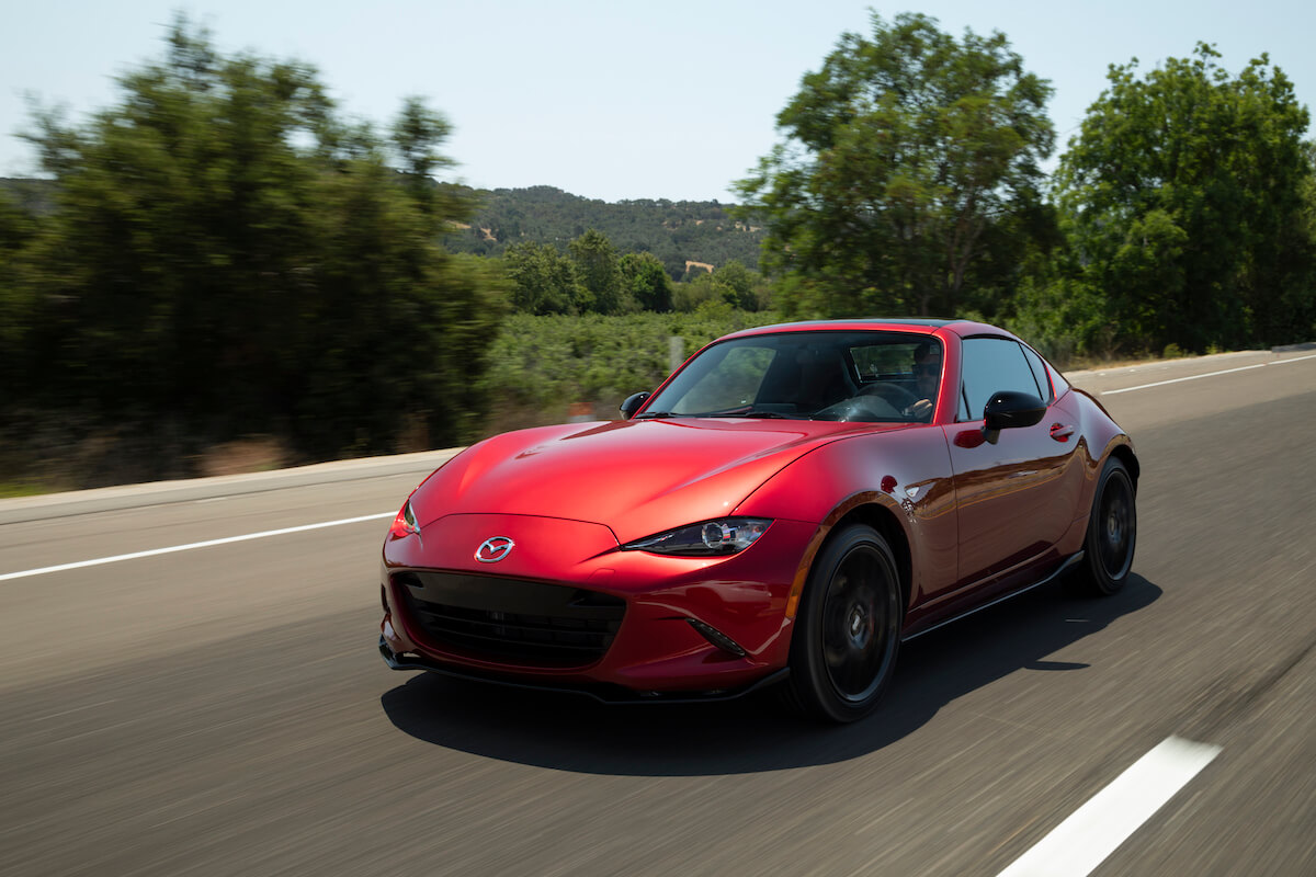 A red 2023 Mazda MX-5 Miata driving on a two lane road