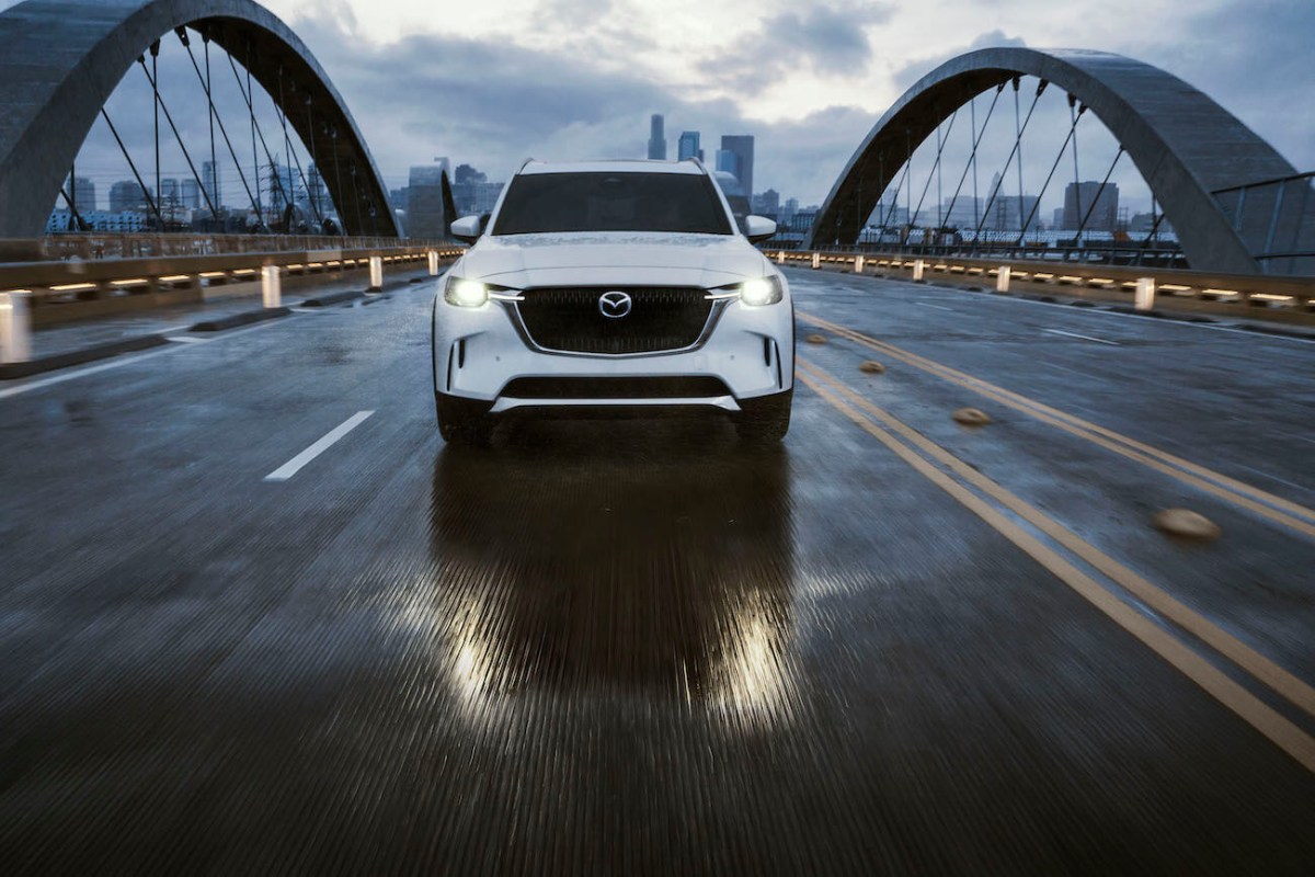 A white 2024 Mazda CX-90 driving on a bridge on a cloudy day.