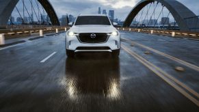 A white 2024 Mazda CX-90 driving on a bridge on a cloudy day.