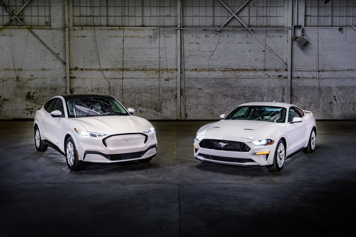 A white set of 2023 Ford Mustang models, the GT and Mach-E, pose in a hangar.