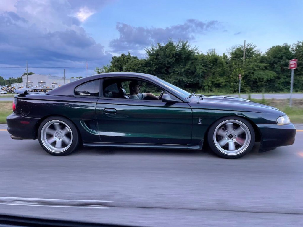 A Mystichrome Ford Mustang Cobra driving down the road