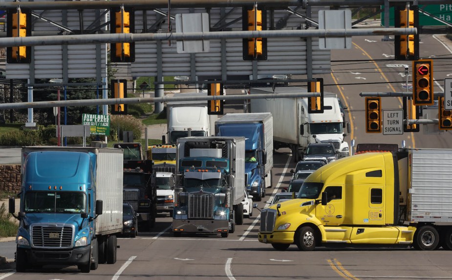 A row of semi-trucks merging on a highway interchange, mixed with regular traffic.