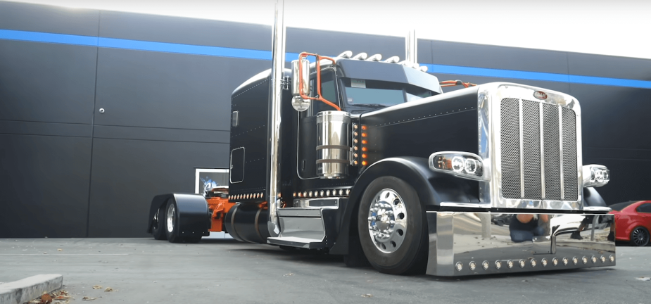 A black Peterbilt Semi-truck customized with chrome, parked in front of a black wall.