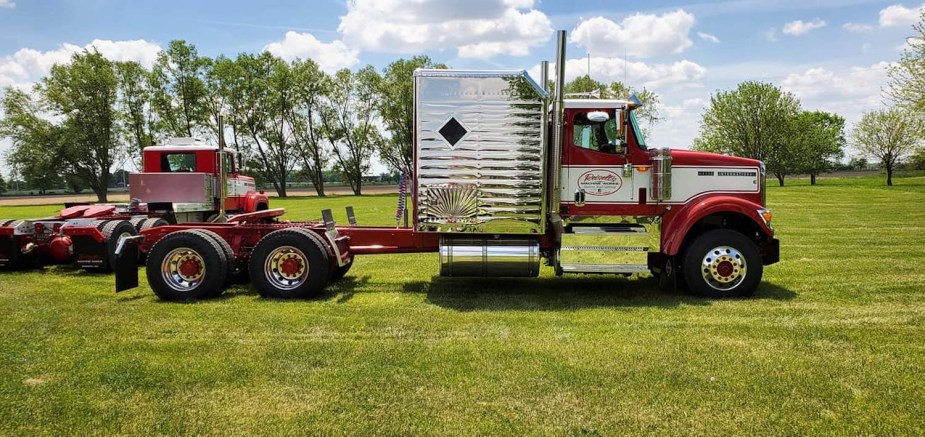 A semi-truck with a retro chrome-plated sleeper parked in a field.