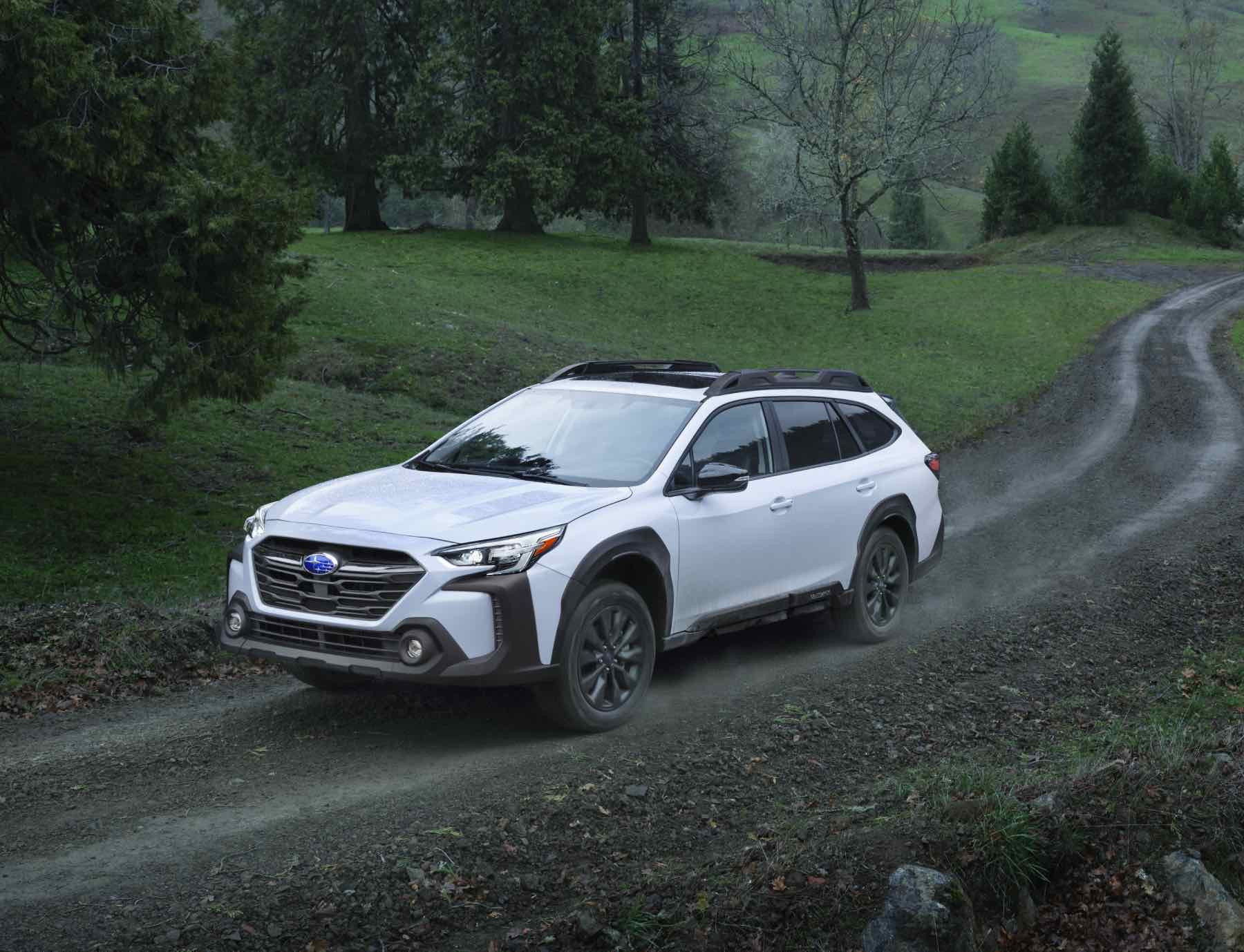 A white 2023 Subaru Outback drives up a muddy road to show its all-terrain strengths.
