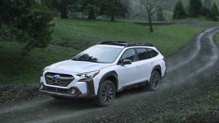 A white 2023 Subaru Outback drives up a muddy road to show its all-terrain strengths.