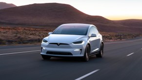 A white 2023 Tesla Model X midsize SUV is driving on the road.