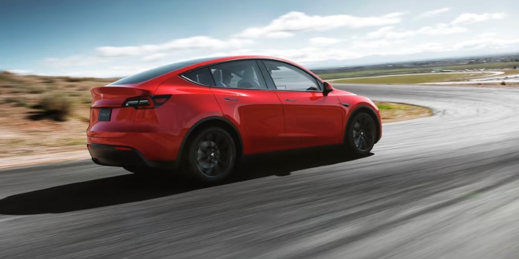 A red 2023 Tesla Model Y small electric SUV is driving.