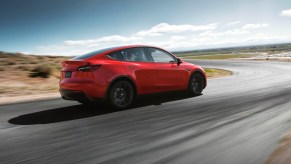 A red 2023 Tesla Model Y small electric SUV is driving on the road.