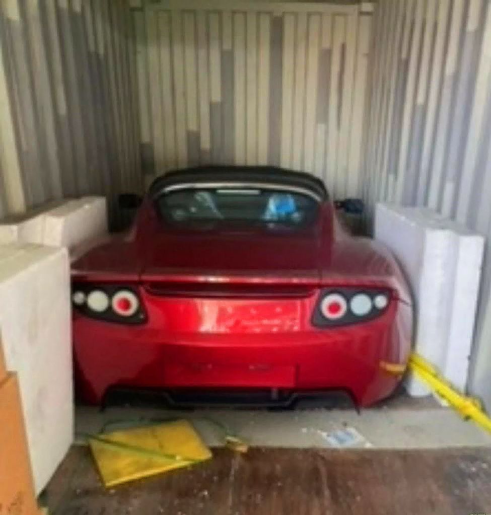 A red Tesla Roadster barn find in a shipping container.