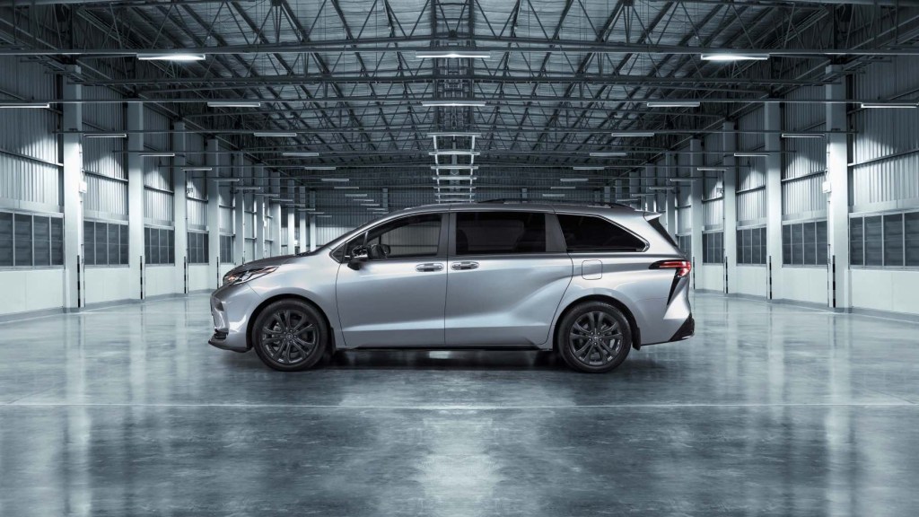 A silver 2023 Toyota Sienna sits in a grey warehouse - side profile view. The Sienna is as practical and efficient as any three-row Toyota SUV.