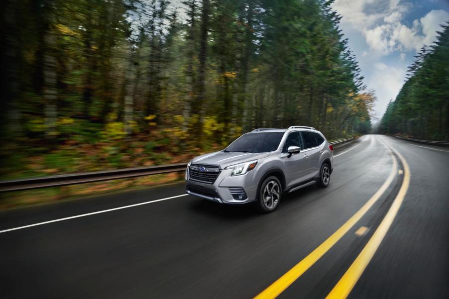 A silver Subaru Forester drivers down a wet road with trees on the side. The Subaru Forester's weakness is that it doesn't have a hybrid option.