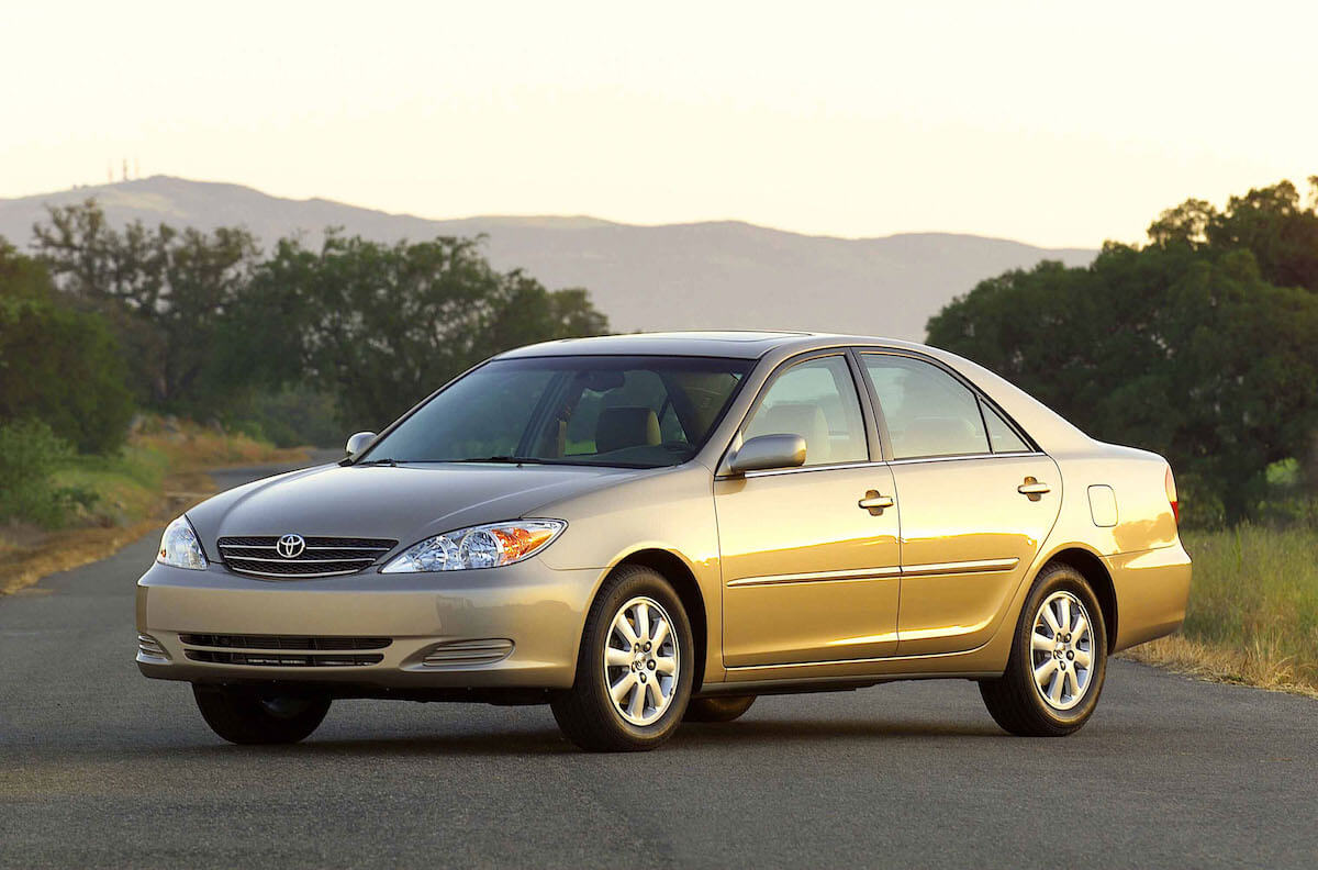 A gold Toyota Camry parked on a single lane road at sunset.