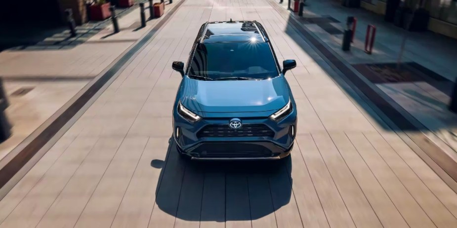 A blue 2023 Toyota RAV4 Hybrid small hybrid SUV is driving on the road. 