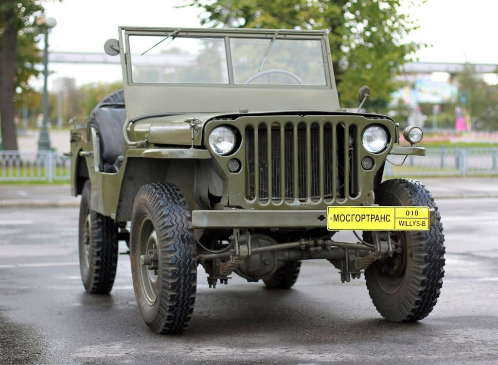 A green Willys Jeep parks at a show. 